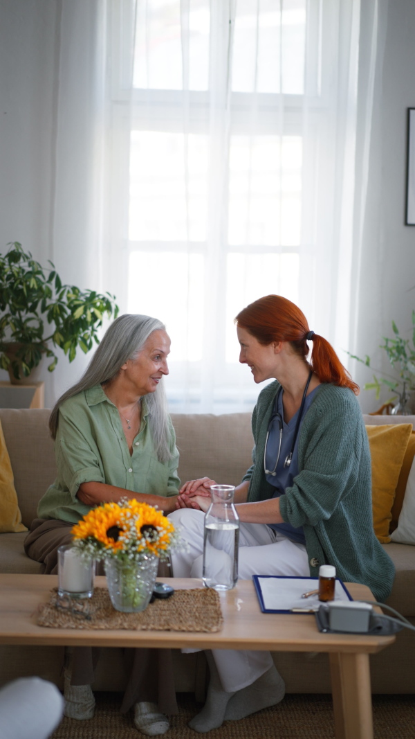 Nurse talking with senior woman, holding her hand and consoling her at her home.