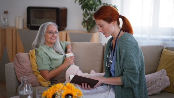 Nurse reading a book to senior woman at her home.