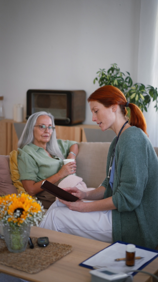 Nurse reading a book to senior woman at her home. Vertical footage.