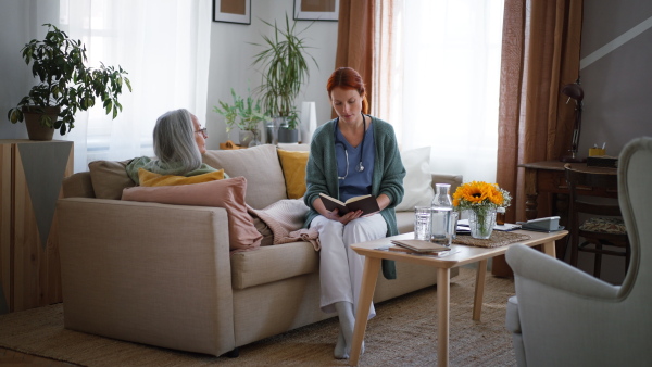 Nurse reading a book to senior woman at her home.