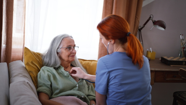 Nurse examining senior patient with stethoscope at home.