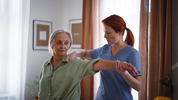 Nurse exercising with senior woman at her home, concept of a healthcare and rehabilitation.