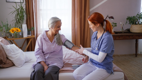 Nurse measuring blood pressuer to senior woman in her home.