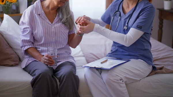 Nurse giving pills to senior woman in her home.