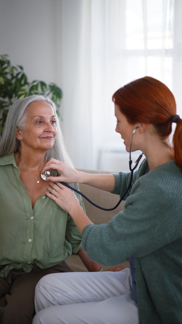 Nurse examining senior patient with stethoscope at her home. Vertical footage.