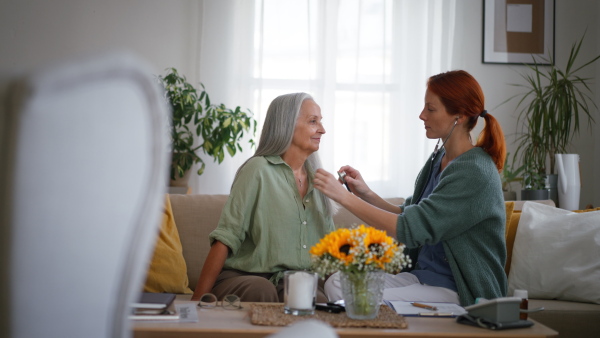 Nurse examining senior patient with stethoscope at home.