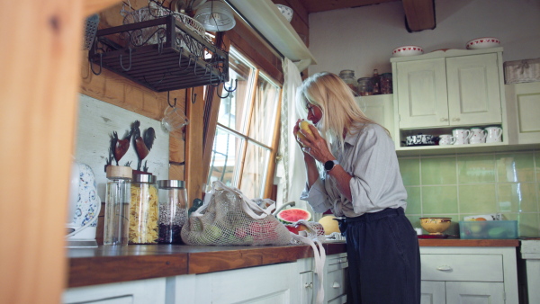 A senior woman unpacking local food in zero waste packaging from bag in kitchen at home.