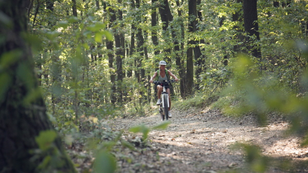 An active senior woman biker cycling outdoors in forest.