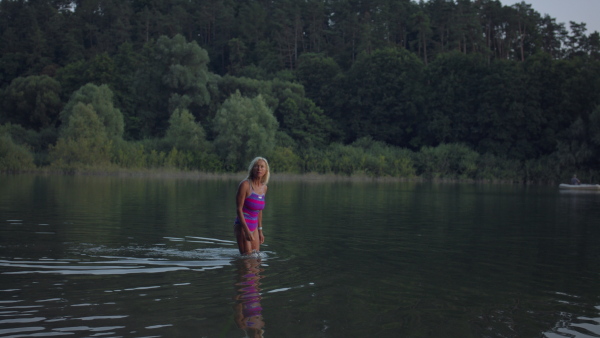 A side view of active senior woman swimmer diving outdoors in lake.