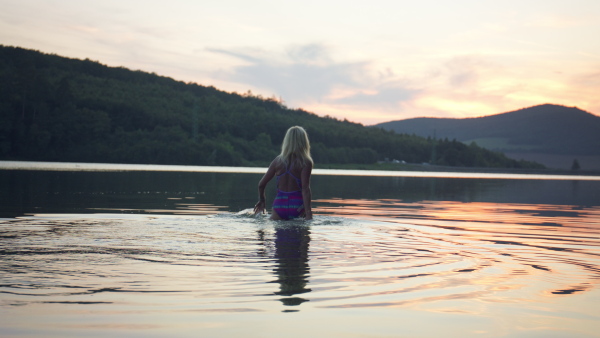 A rear view of active senior woman swimmer diving outdoors in lake.