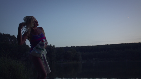 An active senior woman swimmer drying herself with towell outdoors by lake.