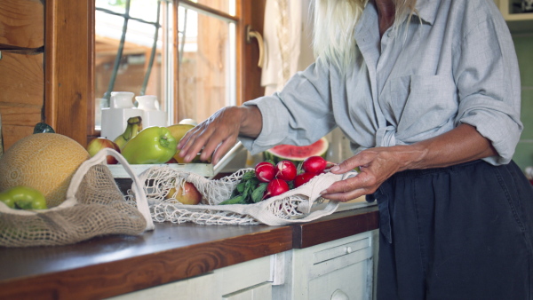 A senior woman unpacking local food in zero waste packaging from bag in kitchen at home.