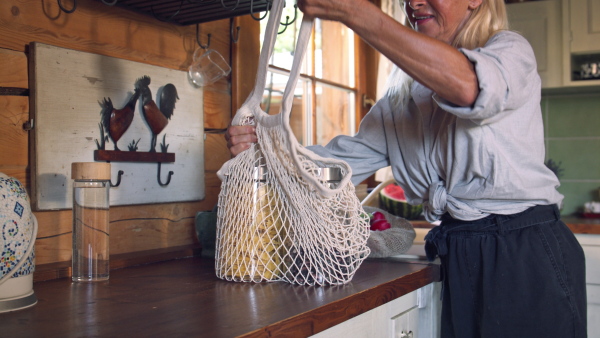 A senior woman unpacking local food in zero waste packaging from bag in kitchen at home.