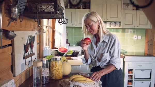 A senior woman unpacking local food in zero waste packaging from bag in kitchen at home.