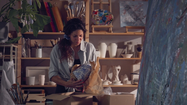 Woman packing pottery products in workshop to send them to customers. Small business concept.