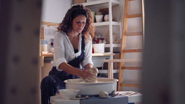 Young female potter working on potters wheel in ceramics studio.