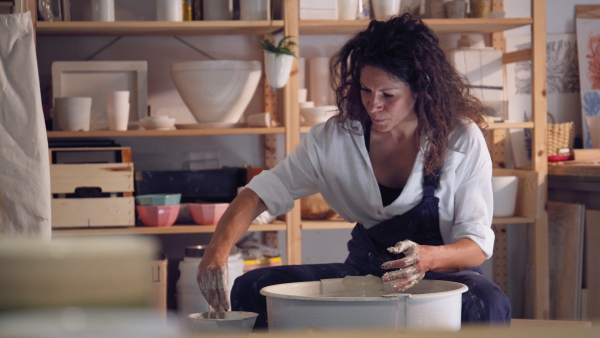 Woman working on potters wheel making clay object in pottery studio.