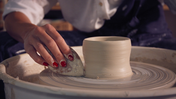 Young female potter working on potters wheel in workshop. Close up.