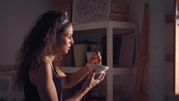 Woman cleaning piece of raw pottery with brush in studio. Dark ambient.