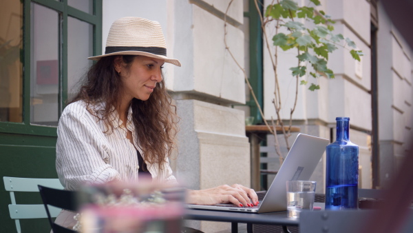 Young woman writing on laptop in outdoor street caffeteria.