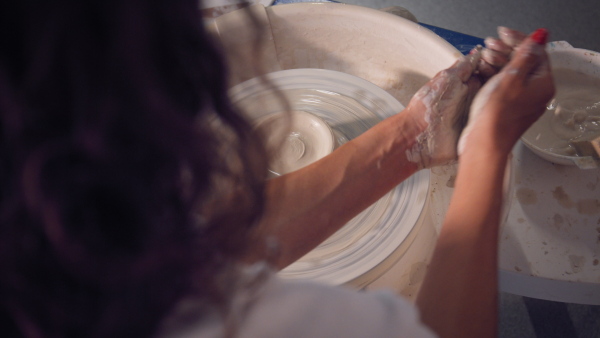 Young female potter working on potters wheel, wetting her hands. Close up.