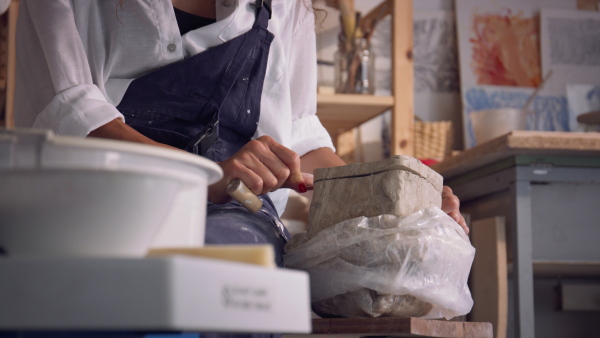 Female potter cutting piece of pottery clay using trimming tool, close-up. Woman using clay wire cutter to a raw piece of clay.