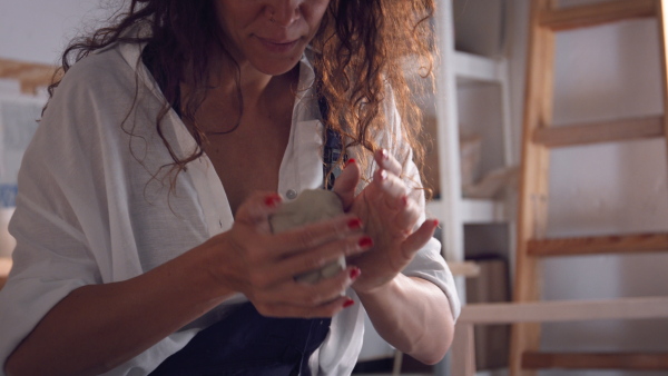 Female potter in workshop preparing clay sitting at spinning wheel.