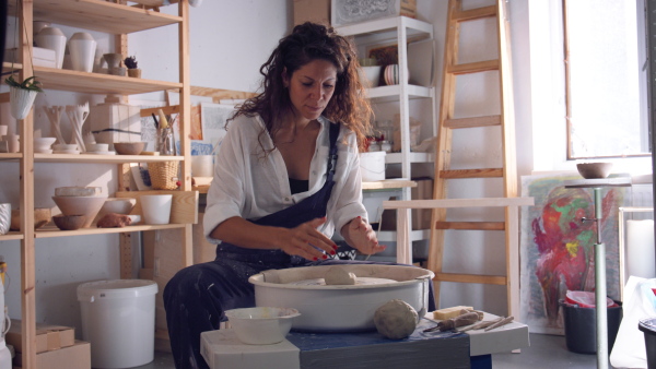 Female potter in ceramics studio working with clay at spinning wheel.