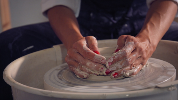 Woman working on potters wheel making clay object in pottery workshop. Close-up.