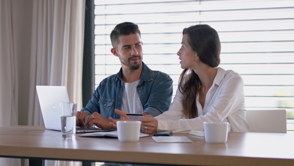 Young couple at home, sitting at table, planning finances, using laptop.