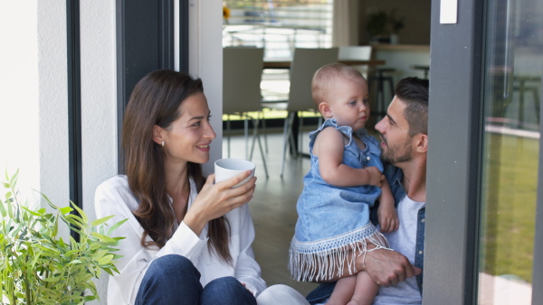 Young mother and father with baby daughter enjoying morning coffee at home on balcony.