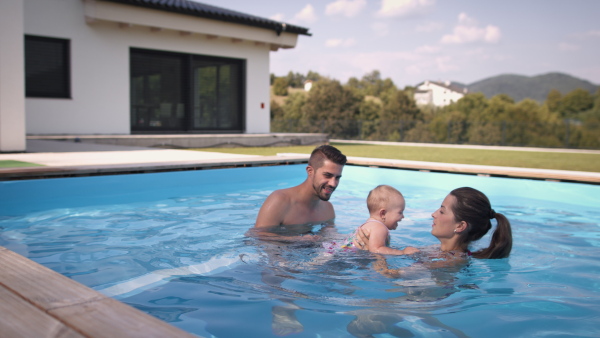 Young mother and father playing with baby girl in garden swimming pool.