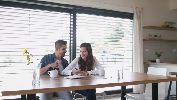 Young couple at home, siting at table, planning finances, using mobile phone application.