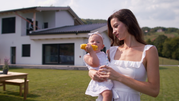 Young mother holding baby girl in arms in front of house.