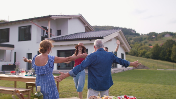 Senior couple welcoming family and friends at summer garden party at their home. Daughter giving present to mother.