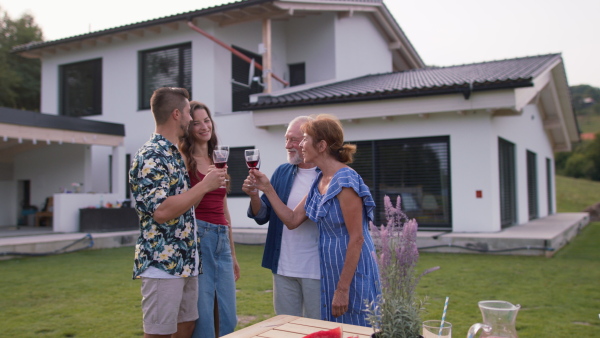 Three generations of family having a summer garden party gathering, modern house in background.