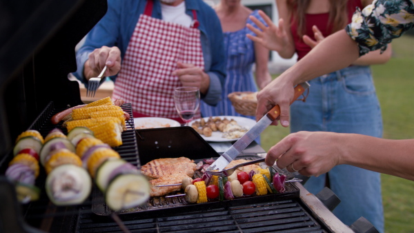 Man preparing food on grill, with his family and friends. Modern house in background. Close up.