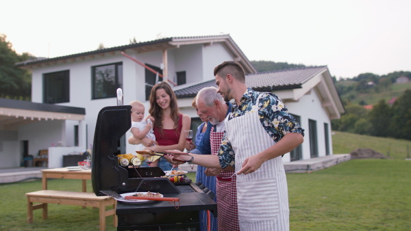 Three generation family having a garden barbeque together. Modern house in background.