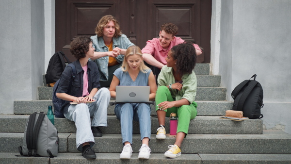 A group of teenagers sitting in outdoor stairs in front of school. Using tablet. Internet and social media addiction among teenagers concept.