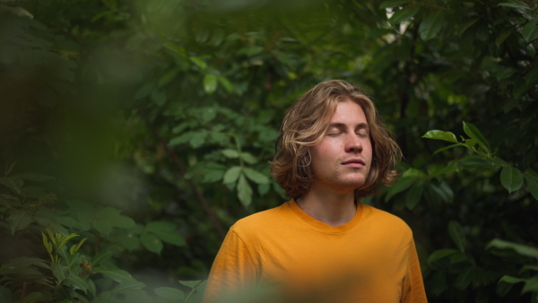 A happy man standing in forest, meditation pose, with closed eyes and smiling.