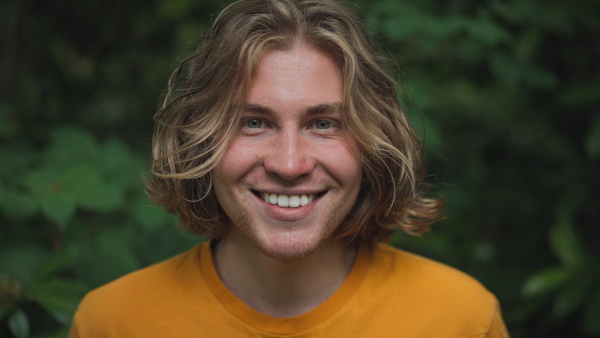 Happy man standing in a forest, looking at camera, smiling.