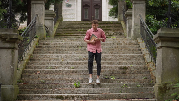 A young man student standing in front of school, holding books, back to school concept.