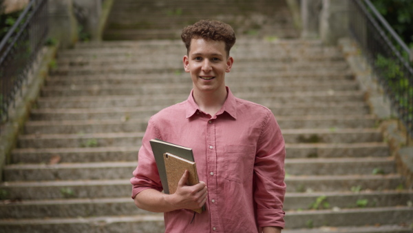 A young man student standing in front of school, holding books, back to school concept.