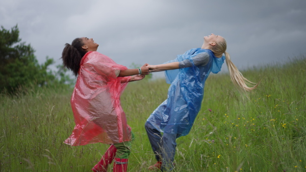 Happy teenage girls wearing raincoats outdoor, standing in a rain. Smiling and enjoying rainy weather.