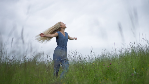 Happy teenage girl dancing at a meadow in rain. Smiling and enjoying rainy weather.