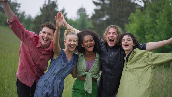 Happy teenage friends wearing raincoats outdoor, standing in a rain. Smiling and enjoying rainy weather.