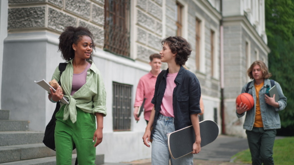 A group of happy teenagers together in front of school, back to school concept.