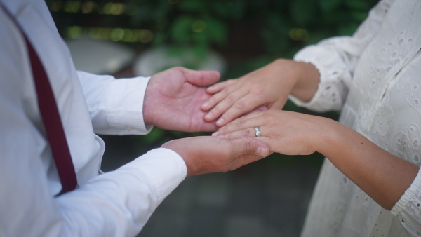 A close-up of bride and groom holding hands with wedding rings at reception outside in the backyard.