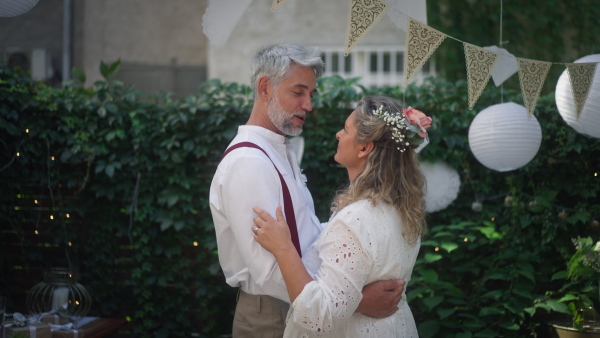 Mature bride and groom dancing together at wedding reception outside in a backyard.