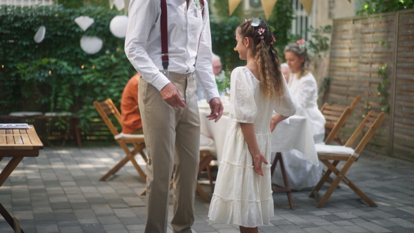 A mature father groom receiving gift from his daughter at wedding reception outside in the backyard.